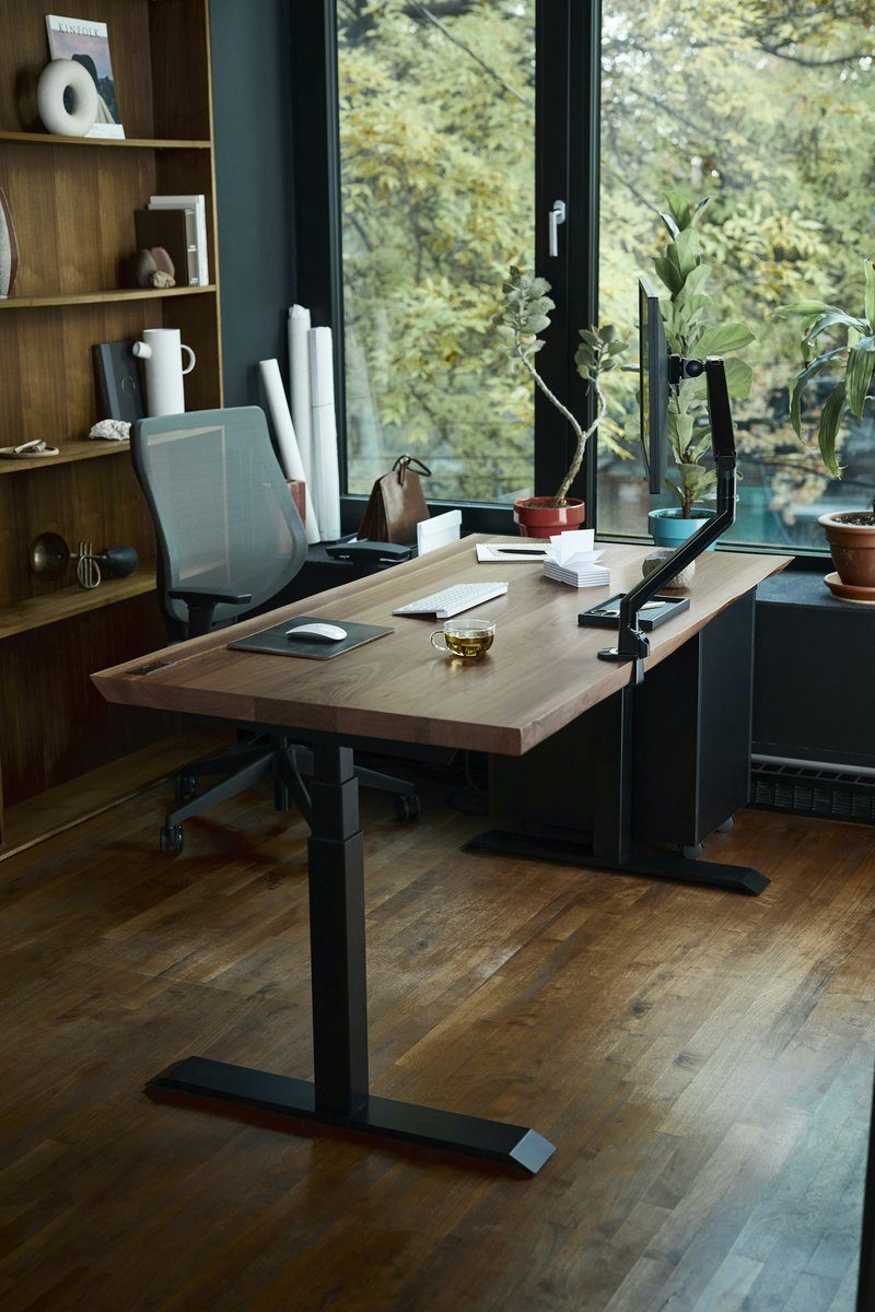 Bureau réglable en hauteur installé près d'une grande fenêtre, sur un parquet clair
