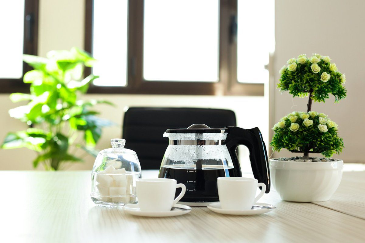 Cafetière, tasses et plantes vertes sur une table de bureau claire