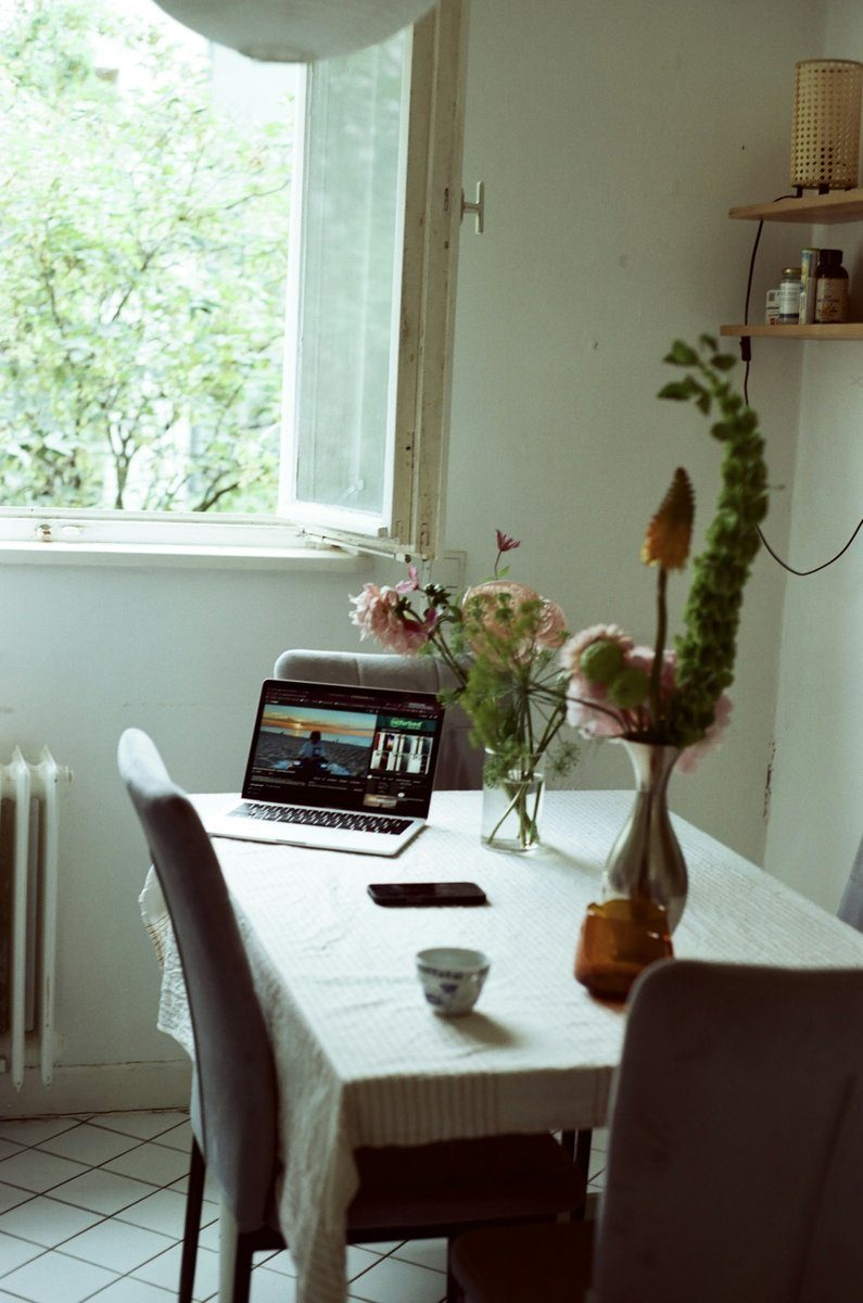 Table de cuisine près d'une fenêtre ouverte, avec un ordinateur portable et un bouquet de fleurs