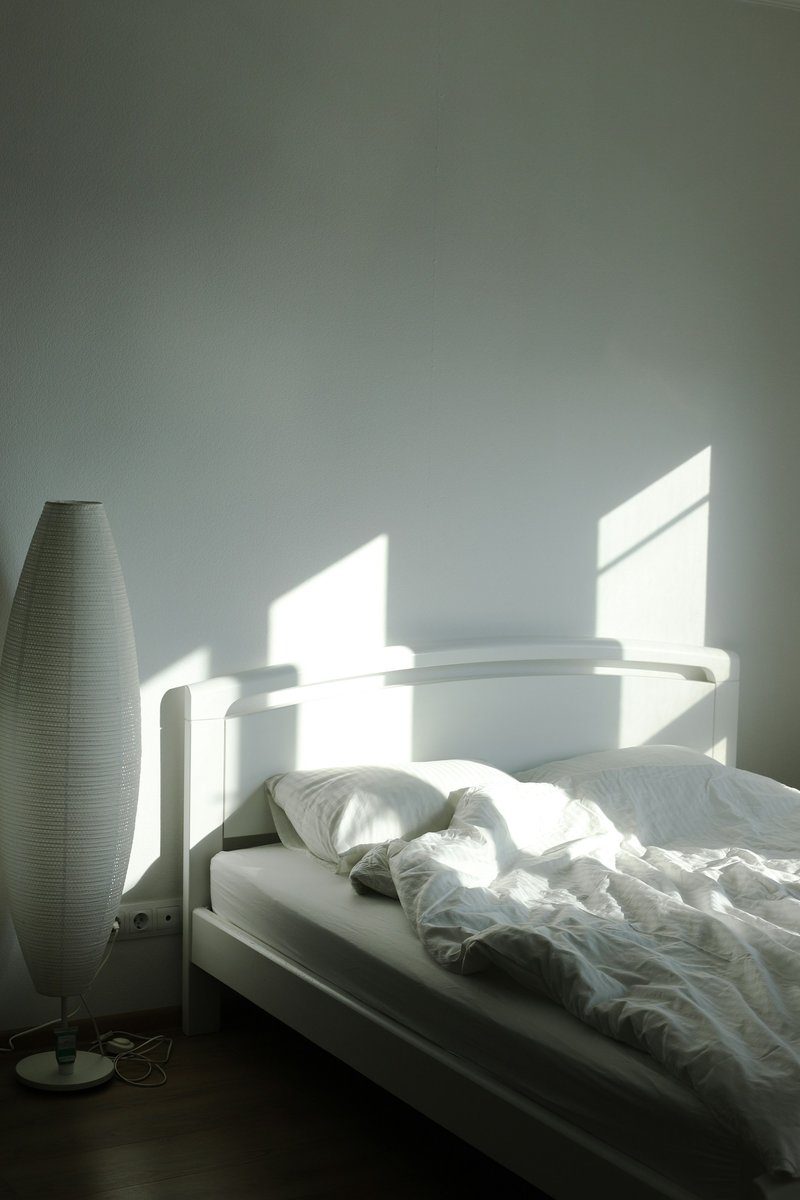 Lit défait dans une chambre blanche traversée par le soleil